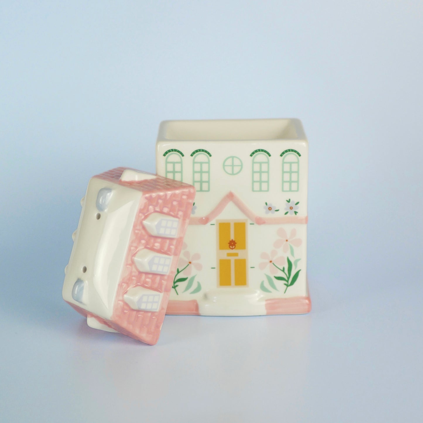 A pastel townhouse wax melt burner with the lid off resting next to the burner