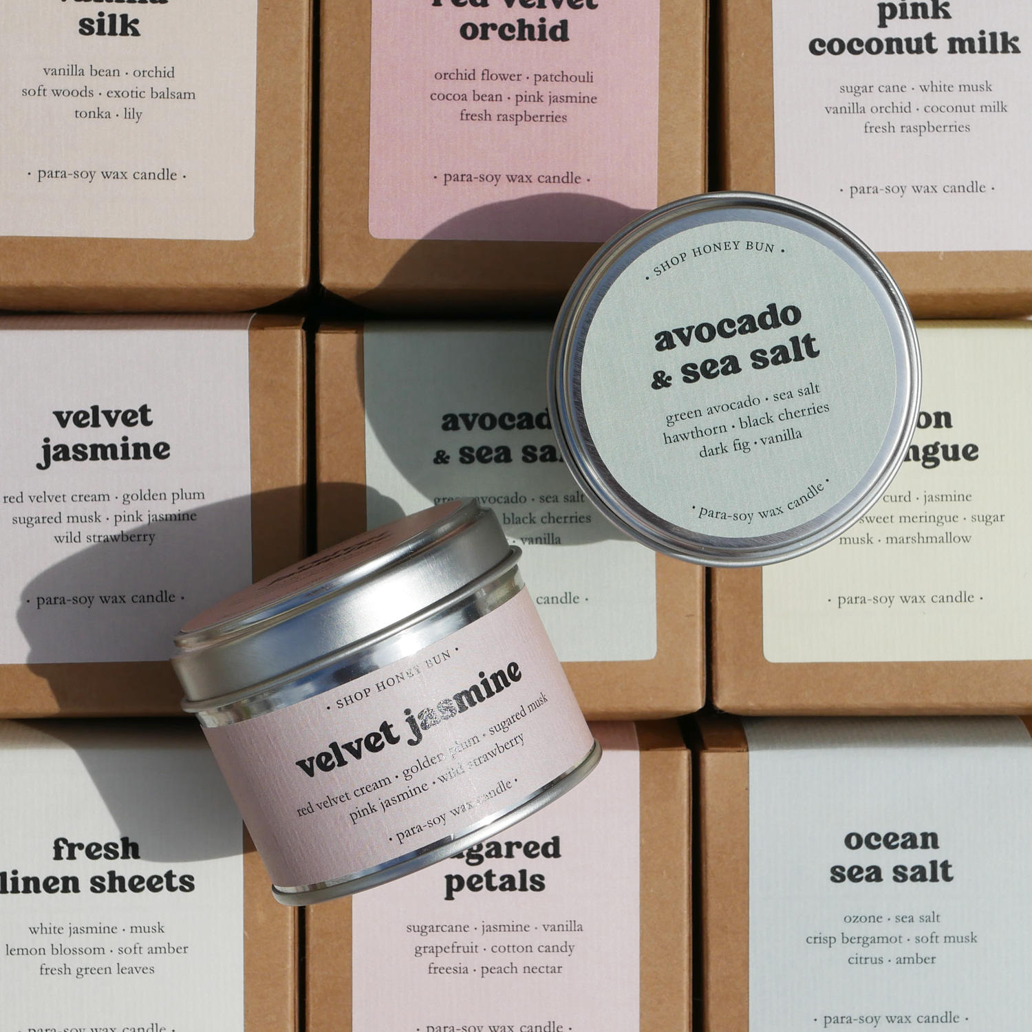 Two scented tin candles on top of scented tin candles in brown kraft boxes with pastel labels