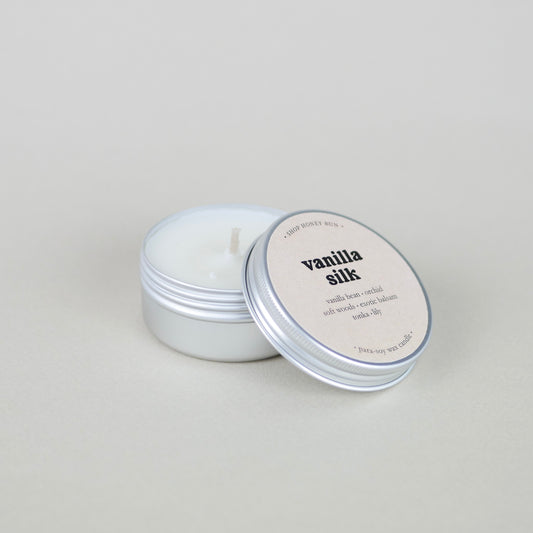 A small sample size vanilla silk scented tin candle with the lid off, showing the candle wick
