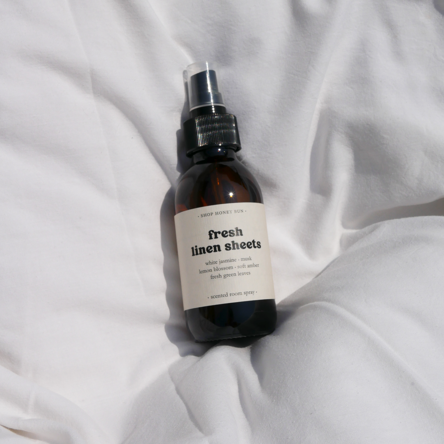 A fresh linen sheets scented room spray in an amber glass spray bottle on a white duvet