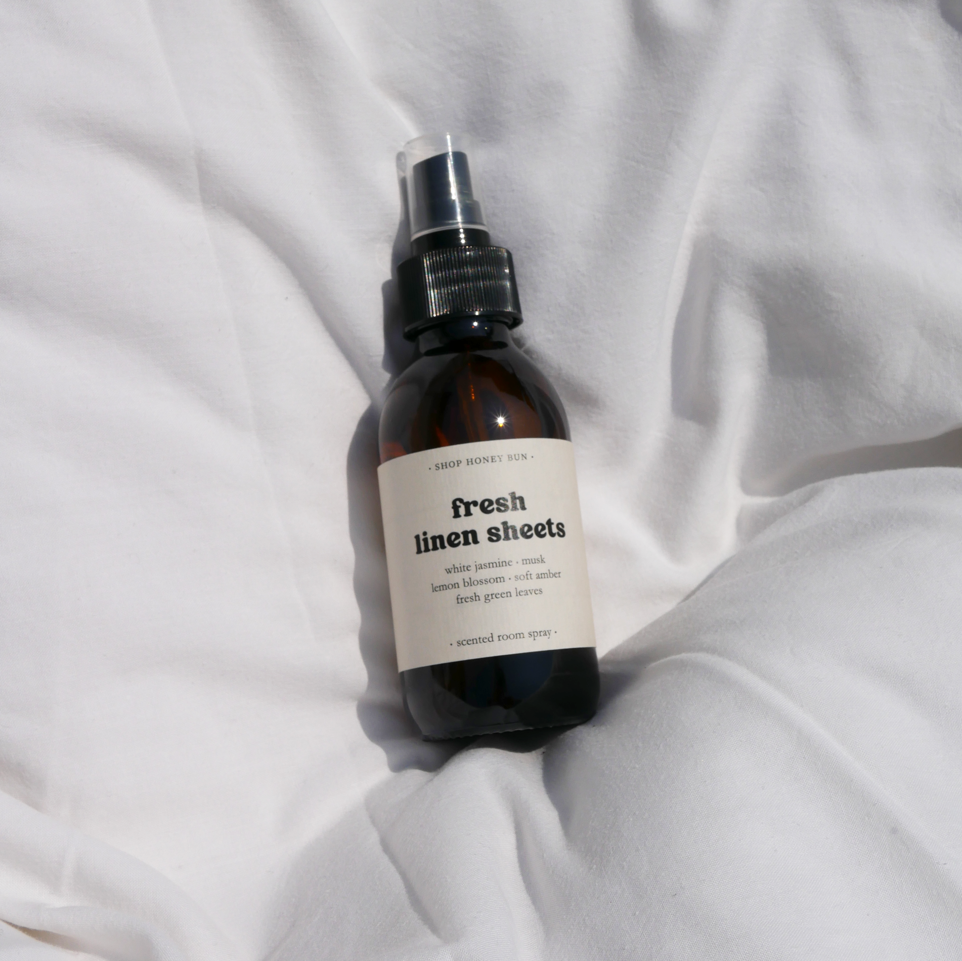 A fresh linen sheets scented room spray in an amber glass spray bottle on a white duvet