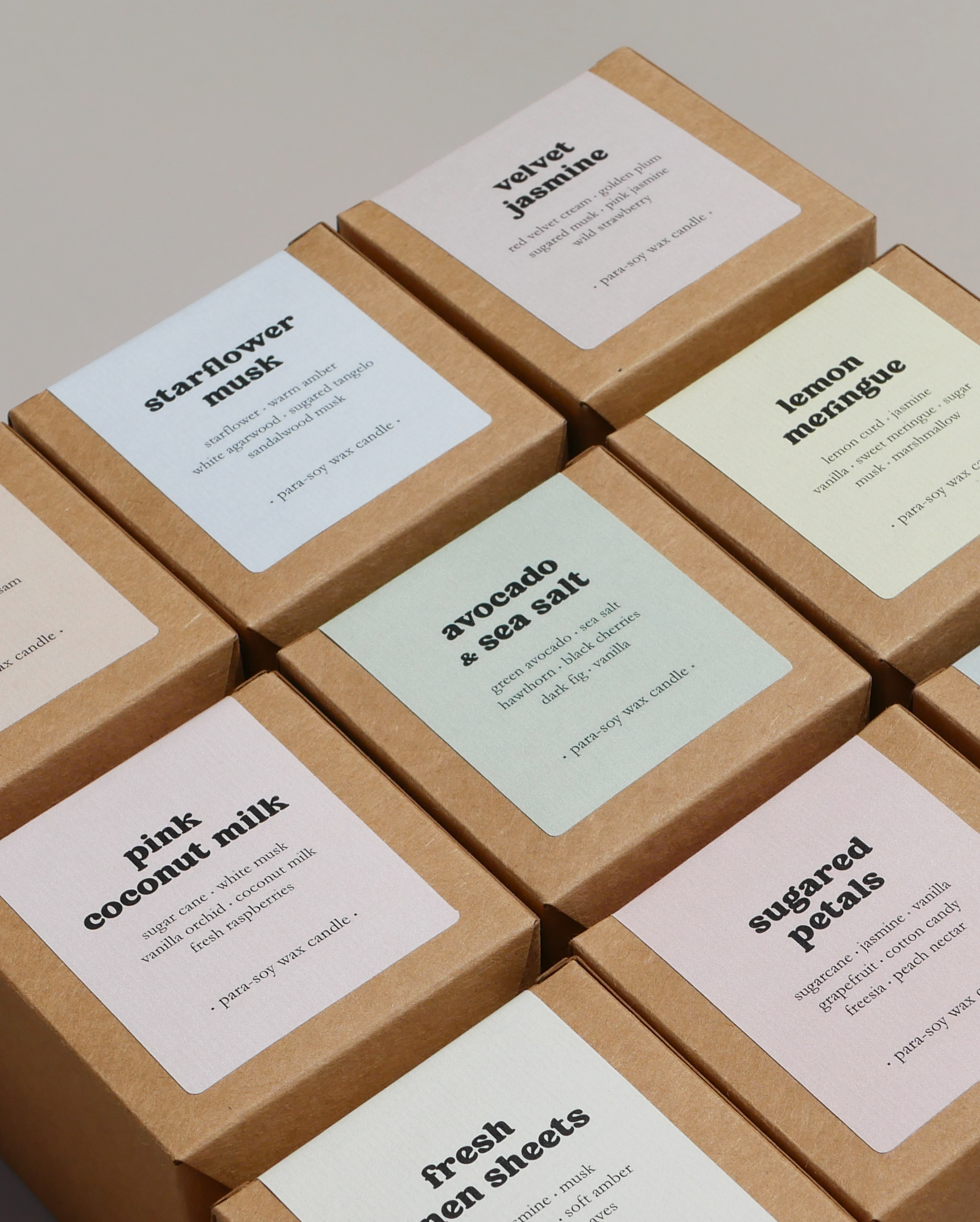 A close up of seven scented candles in brown kraft boxes with pastel paper labels