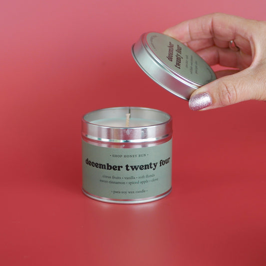 A 30 hour burn time december twenty four scented in candle with a hand lifting off the lid to show the candle wick