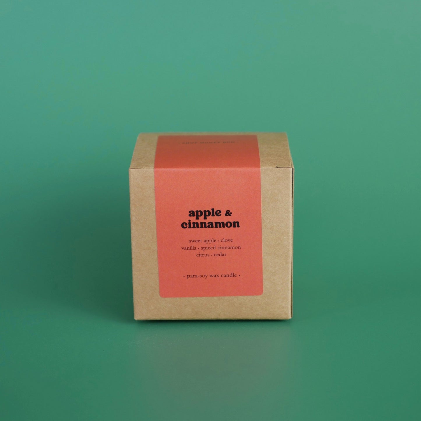 A large apple and cinnamon scented candle in a brown kraft box with a red paper label