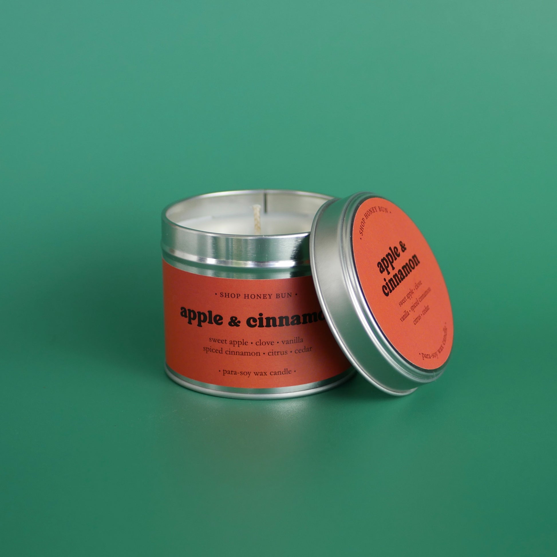 A large apple and cinnamon scented tin candle with the lid off, resting against the candle