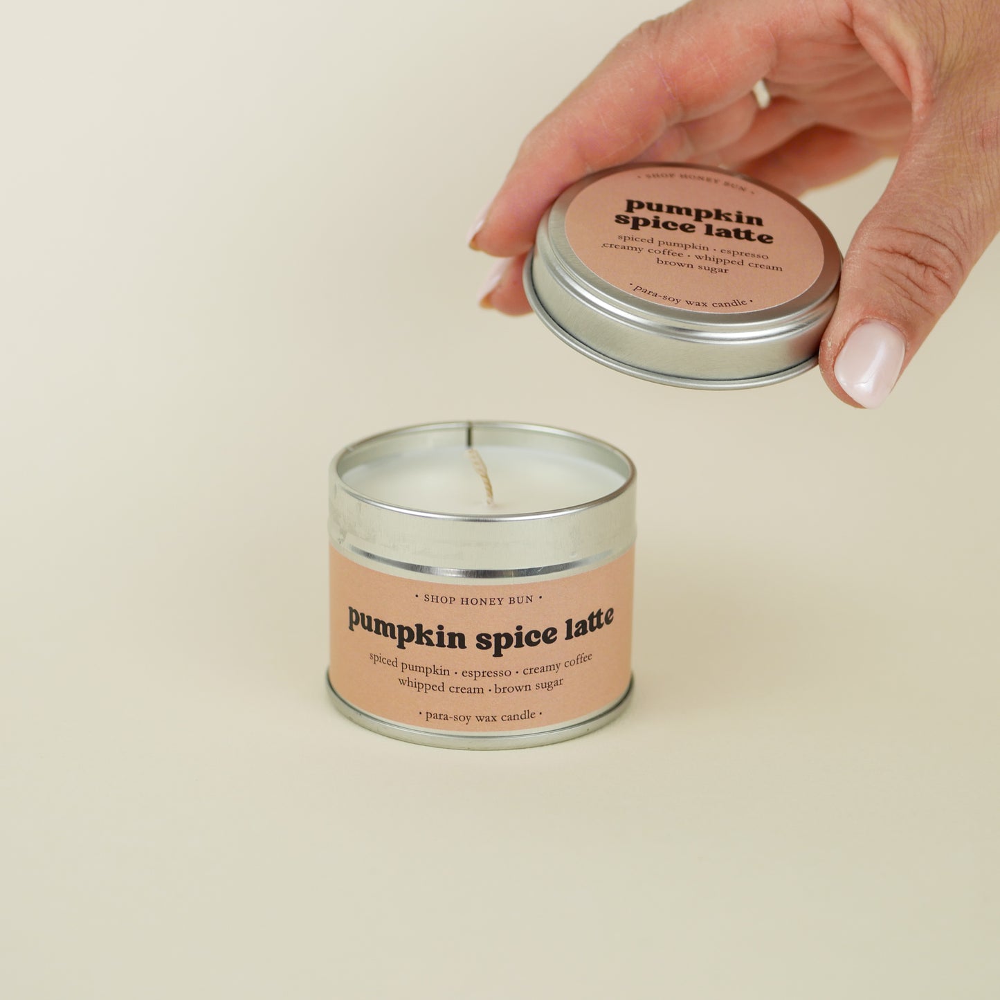 A 20 hour burn time pumpkin spice latte scented in candle with a hand lifting off the lid to show the candle wick
