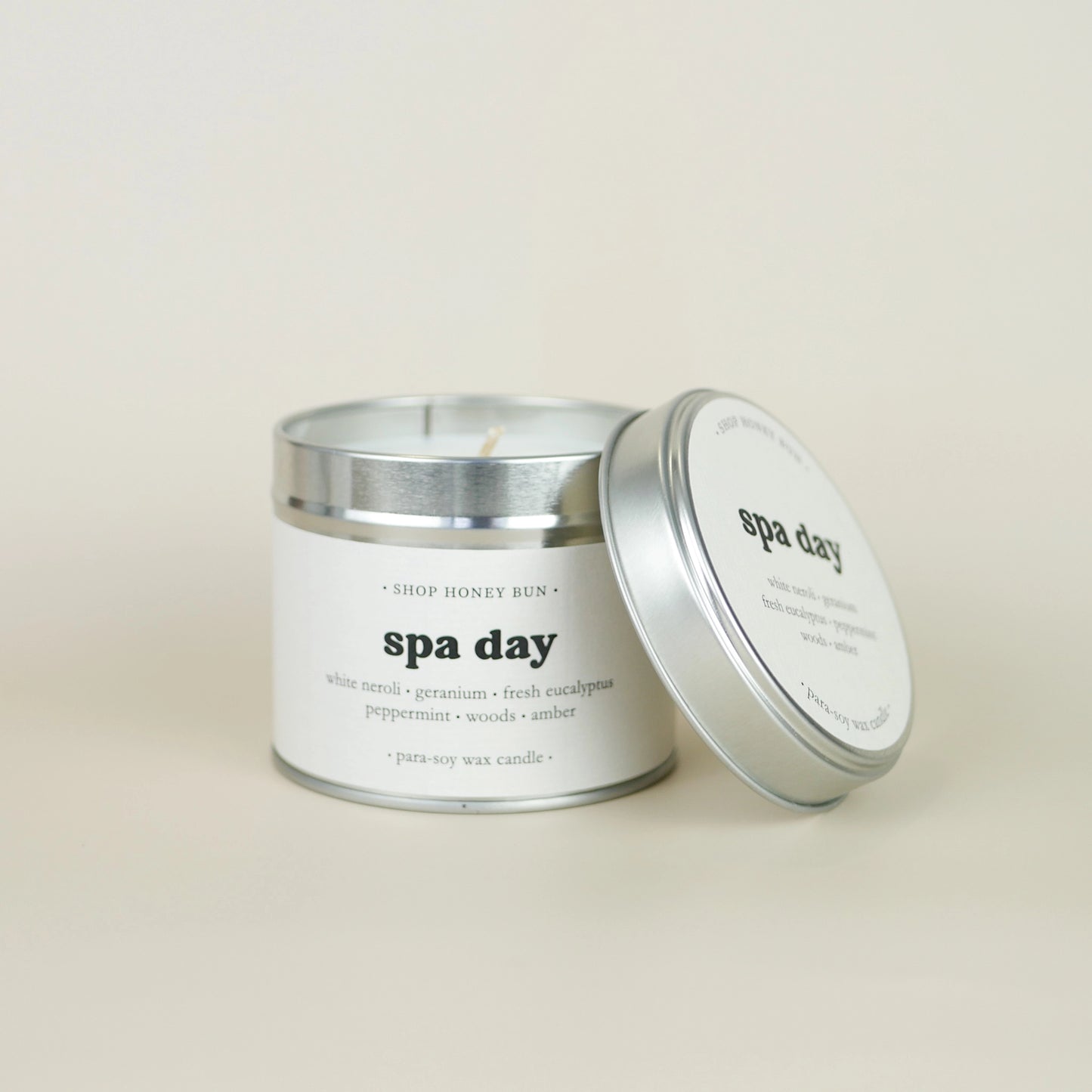 A 30 hour burn time spa day scented tin candle with the lid off, resting on the side of the candle