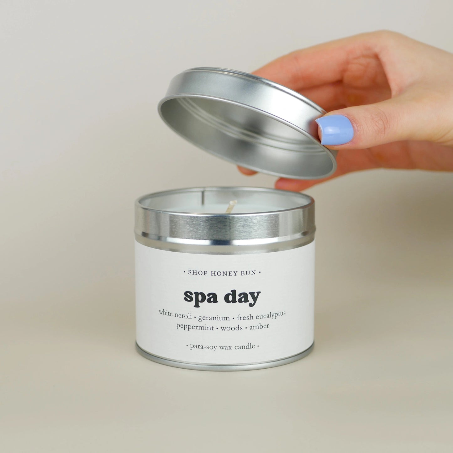 A 30 hour burn time spa day scented in candle with a hand lifting off the lid to show the candle wick
