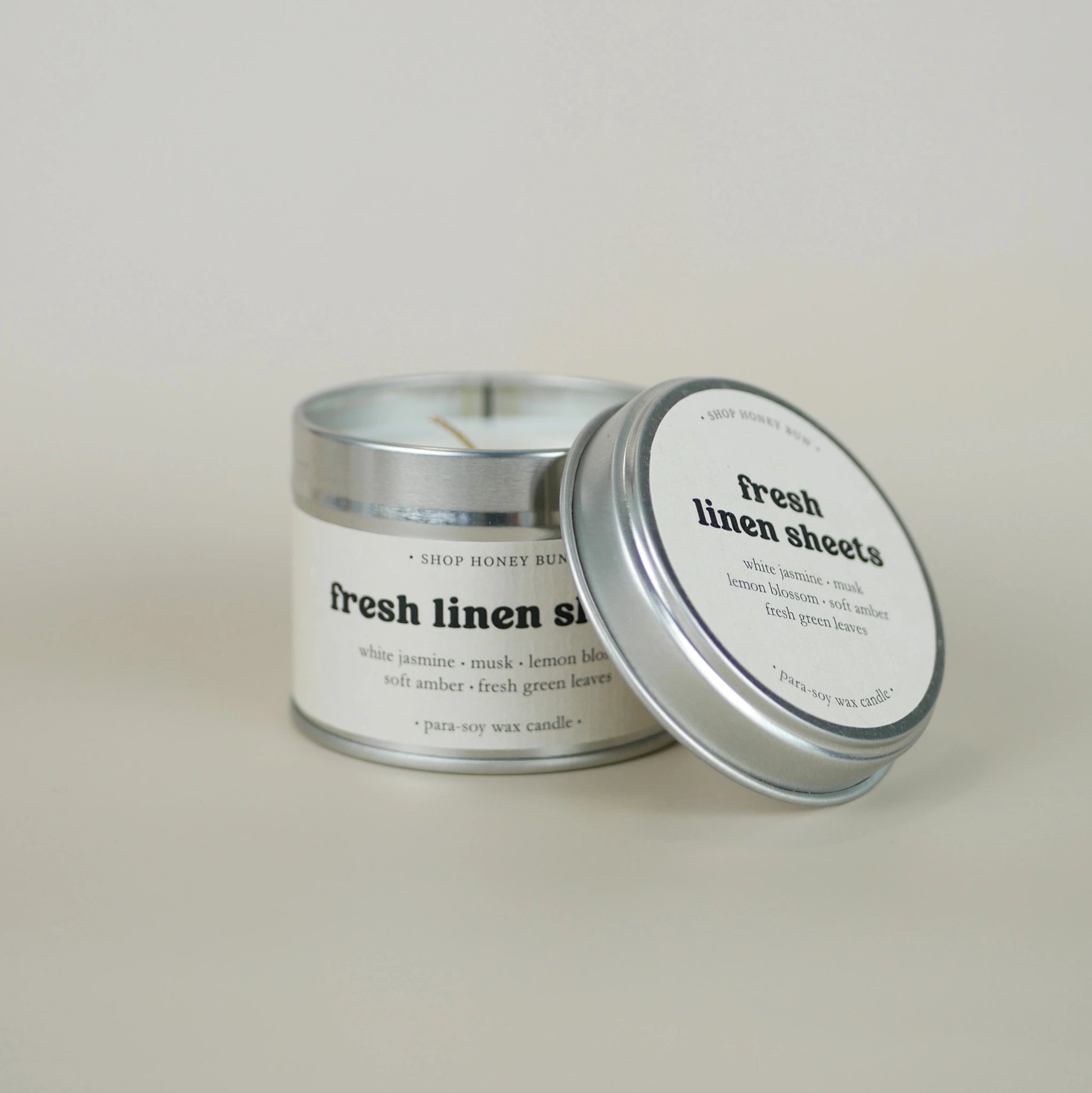 A 20 hour burn time fresh linen sheets scented tin candle with the lid off, resting on the side of the candle
