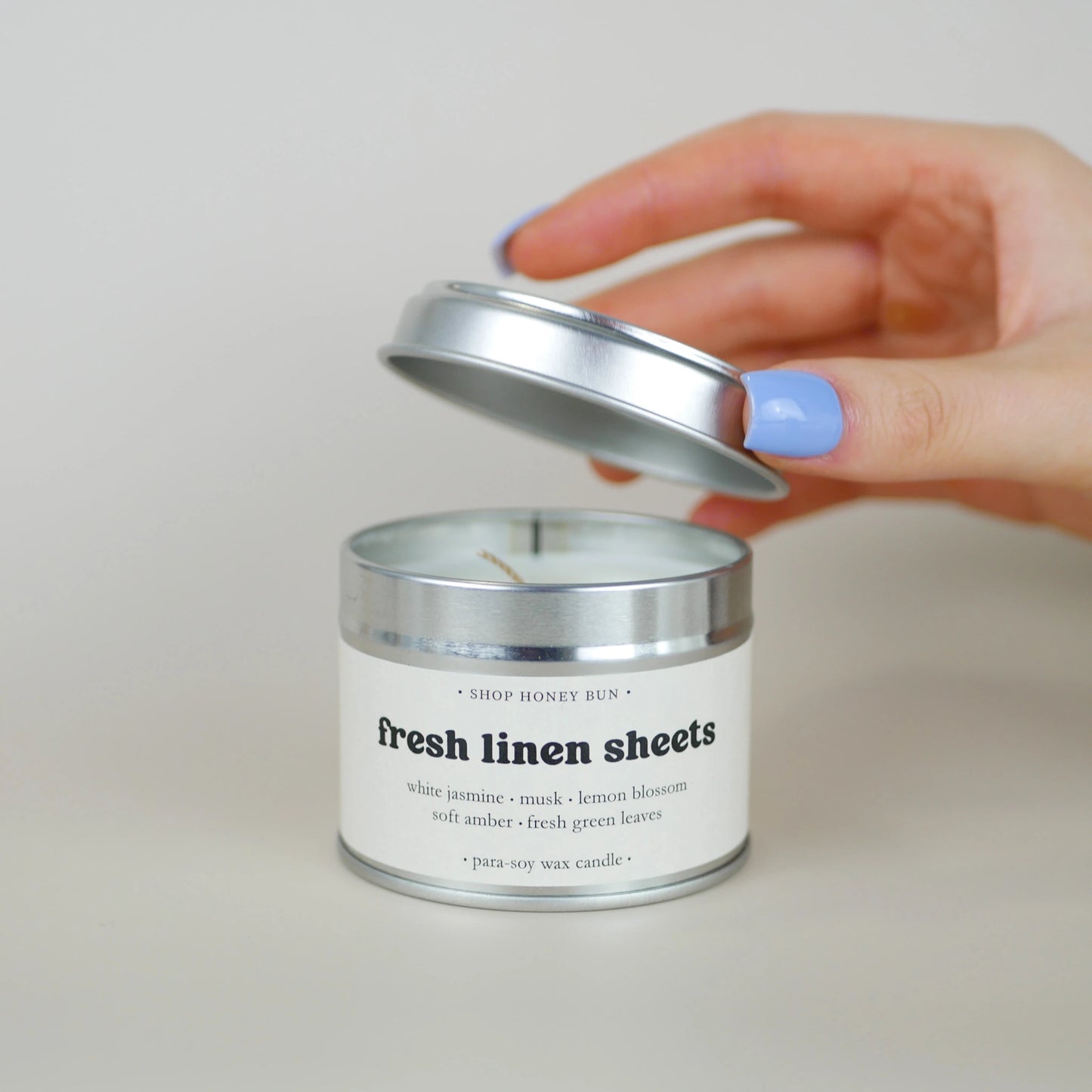 A 20 hour burn time fresh linen sheets scented in candle with a hand lifting off the lid to show the candle wick
