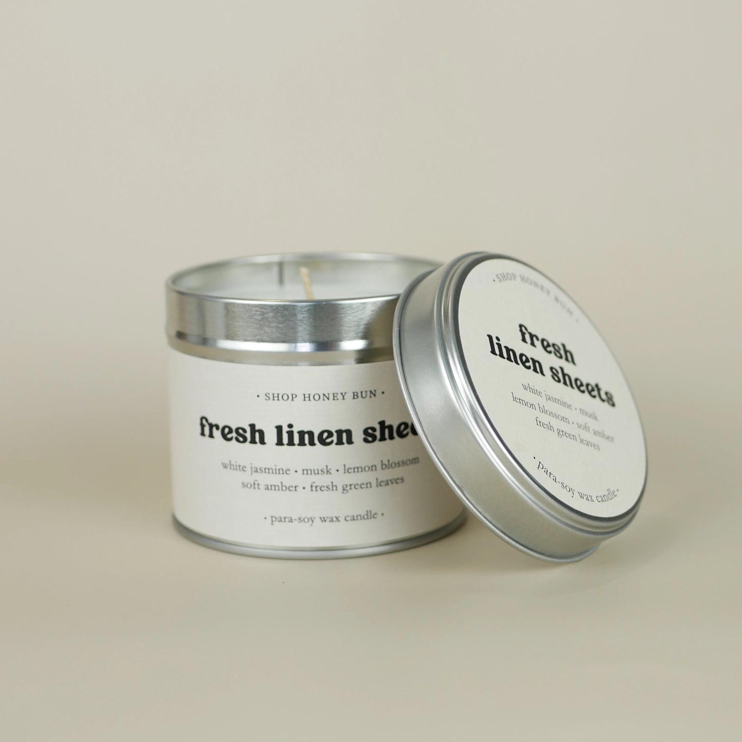 A 20 hour burn time fresh linen sheets scented tin candle with the lid off, resting on the side of the candle
