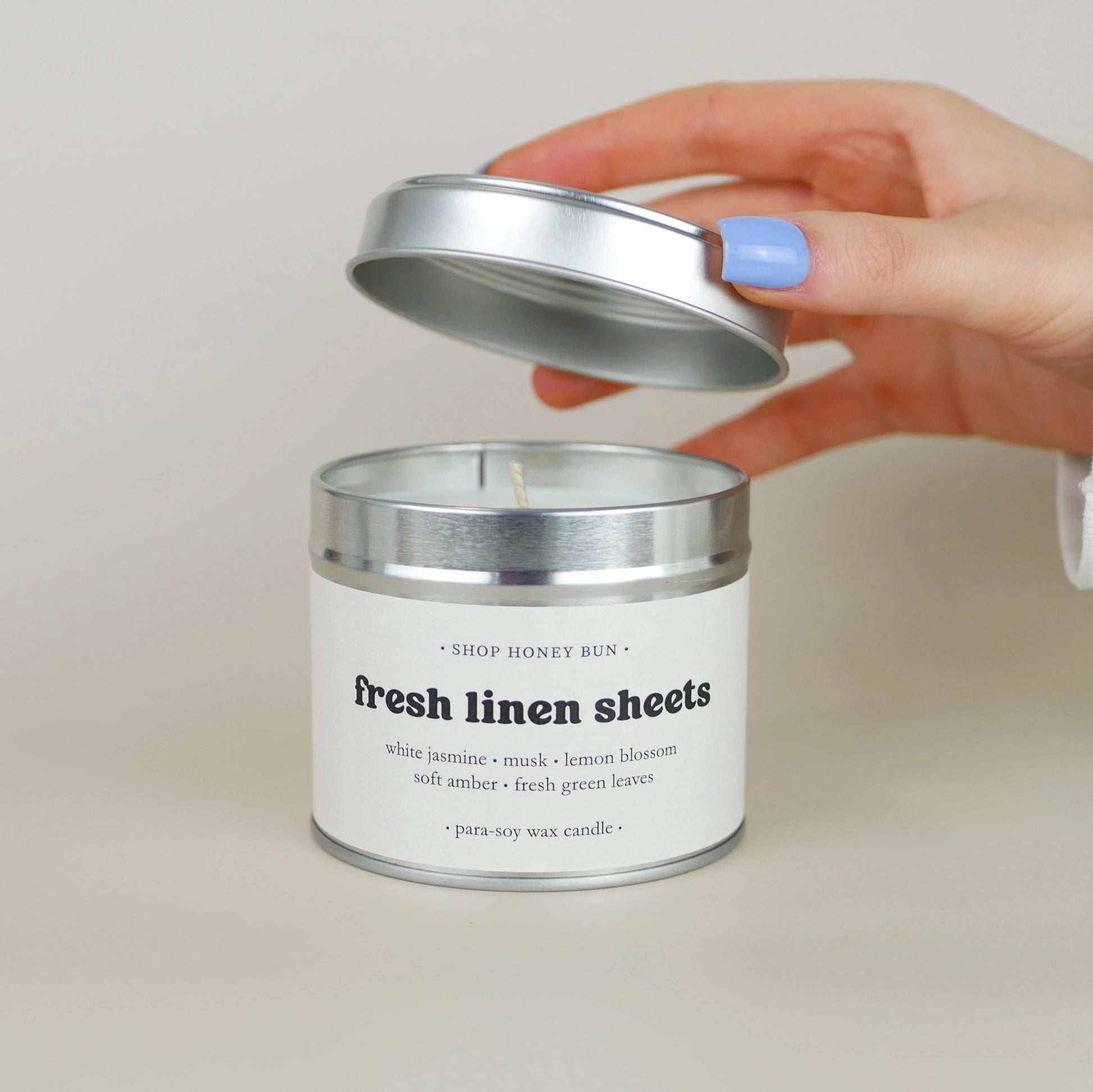 A 30 hour burn time fresh linen sheets scented in candle with a hand lifting off the lid to show the candle wick
