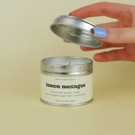 A 20 hour burn time lemon meringue scented in candle with a hand lifting off the lid to show the candle wick

