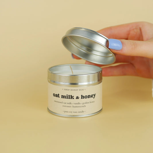 A 20 hour burn time oat milk and honey scented in candle with a hand lifting off the lid to show the candle wick