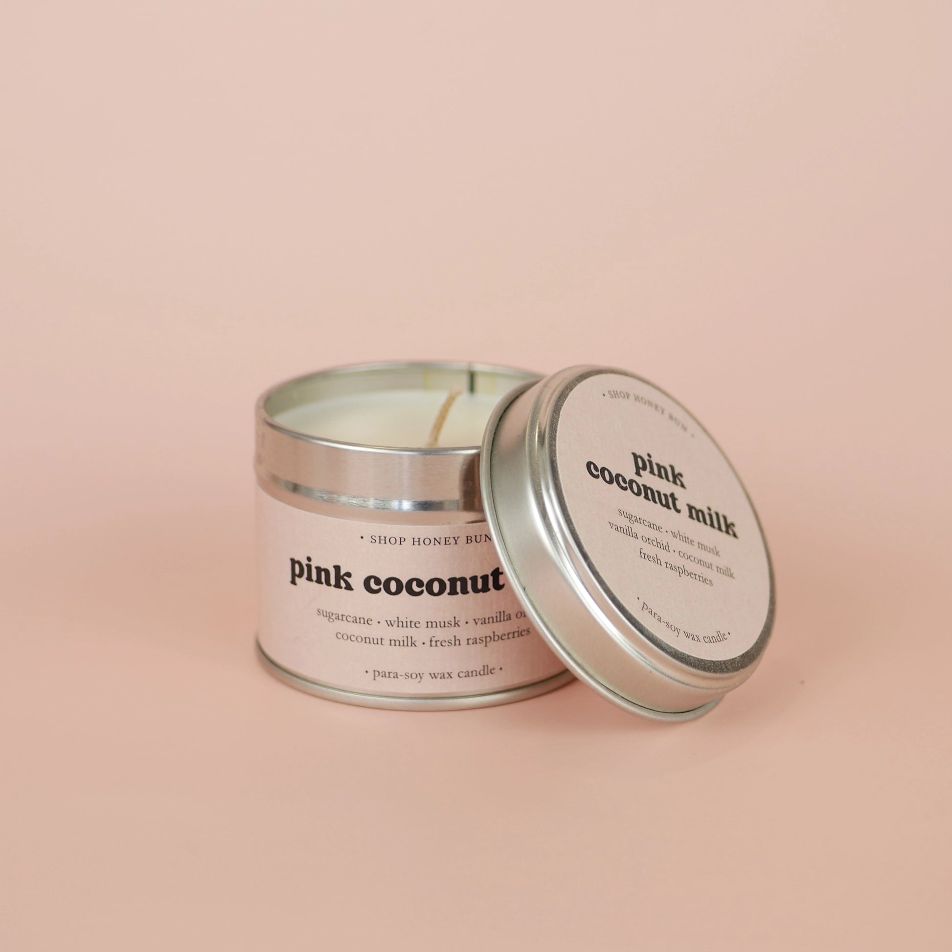 A 20 hour burn time pink coconut milk scented tin candle with the lid off, resting on the side of the candle