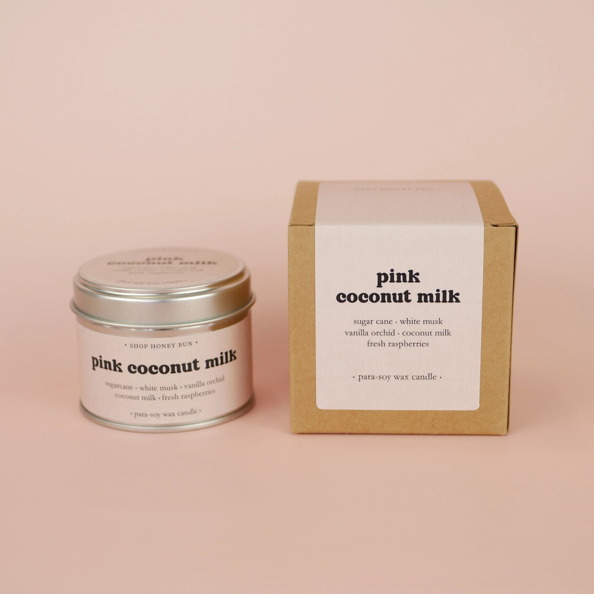 A 20 hour burn time pink coconut milk scented tin candle next to a brown kraft box with a pale pink paper label