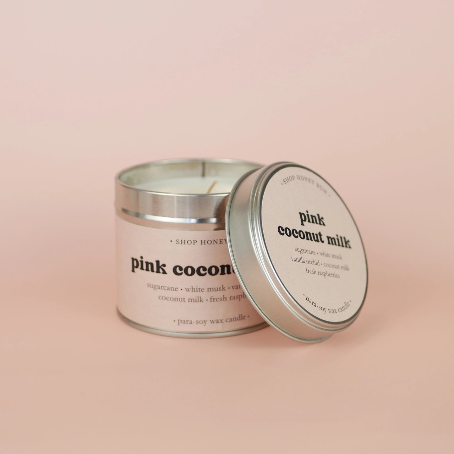 A 30 hour burn time pink coconut milk scented tin candle with the lid off, resting on the side of the candle