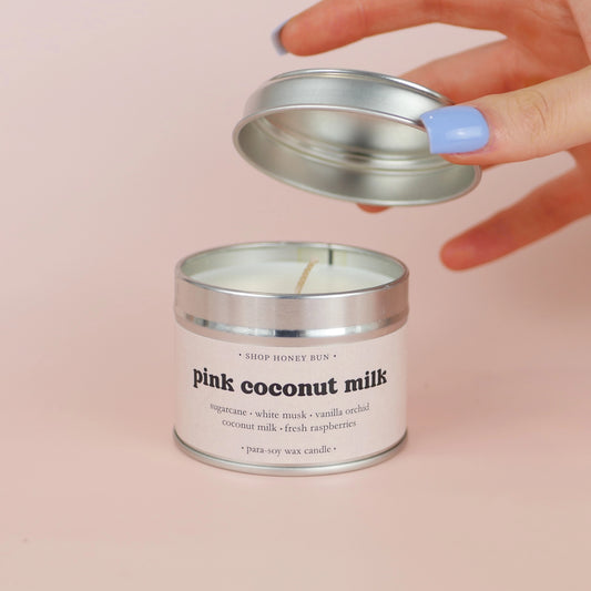 A 20 hour burn time pink coconut milk scented in candle with a hand lifting off the lid to show the candle wick
