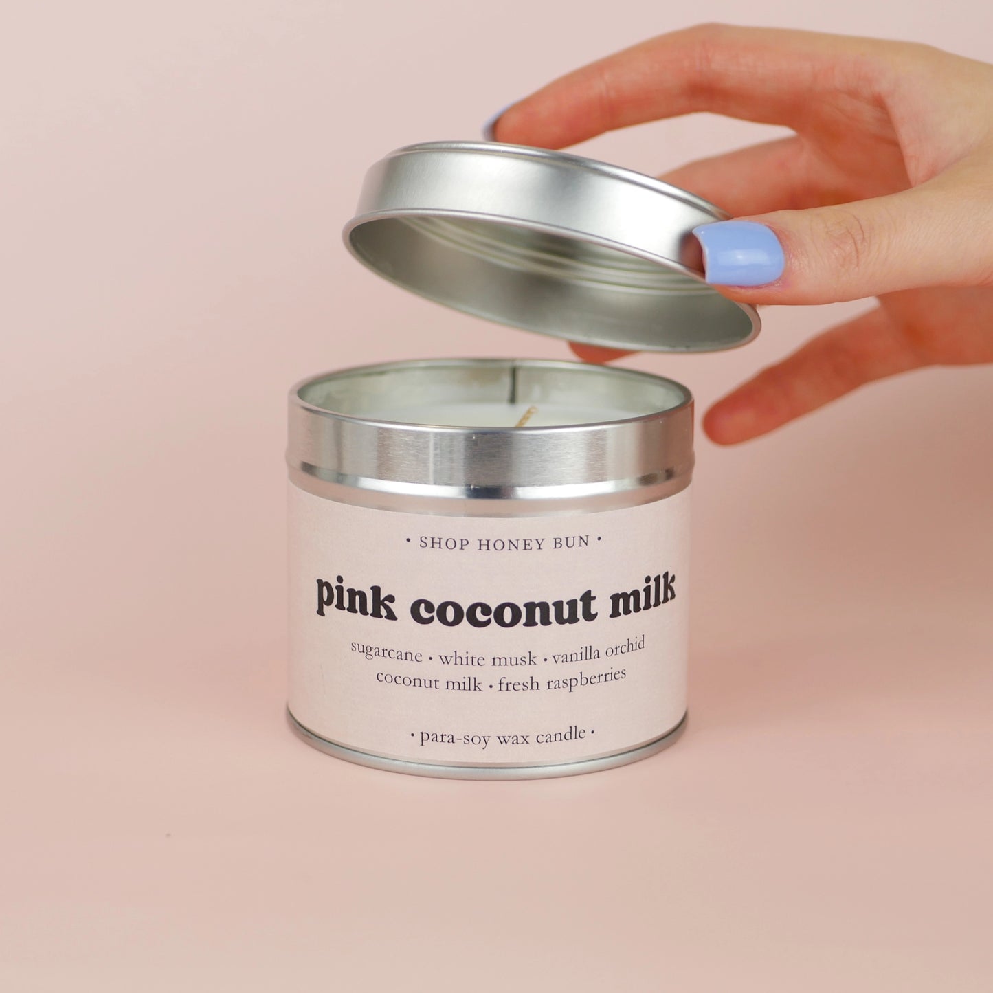 A 30 hour burn time pink coconut milk scented in candle with a hand lifting off the lid to show the candle wick
