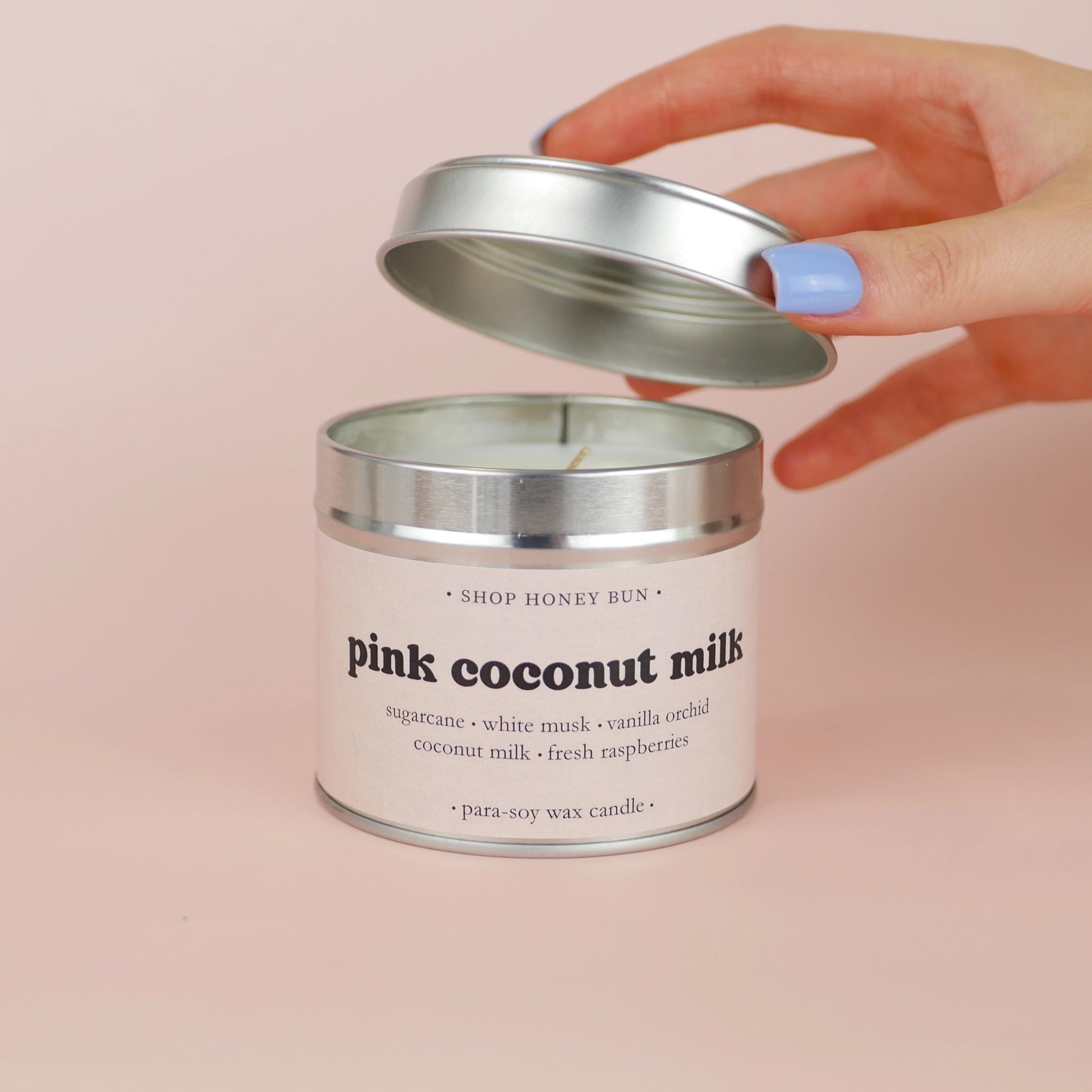 A 30 hour burn time pink coconut milk scented in candle with a hand lifting off the lid to show the candle wick
