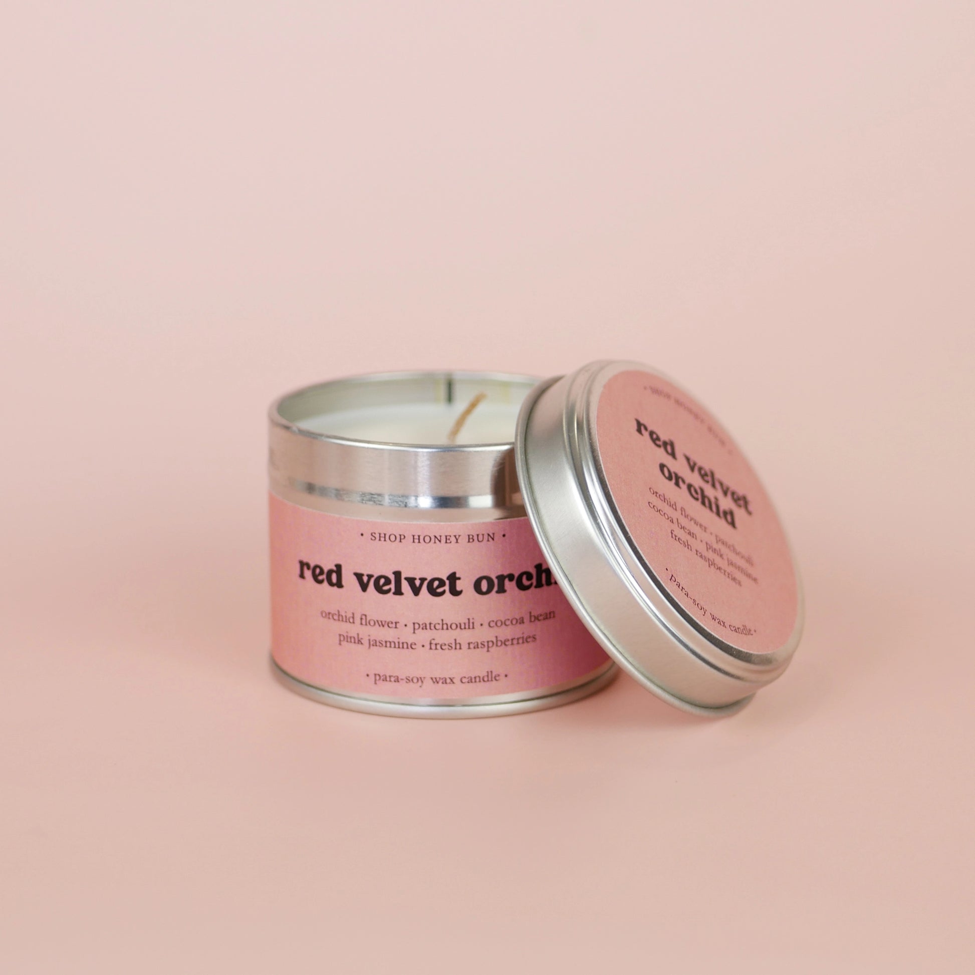 A 20 hour burn time red velvet orchid scented tin candle with the lid off, resting on the side of the candle
