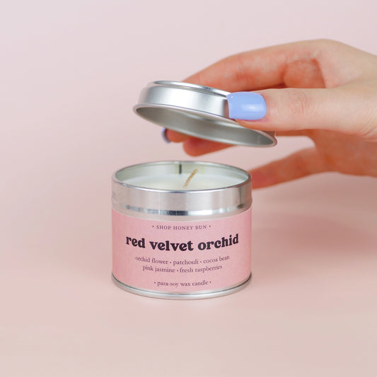 A 20 hour burn time red velvet orchid scented in candle with a hand lifting off the lid to show the candle wick
