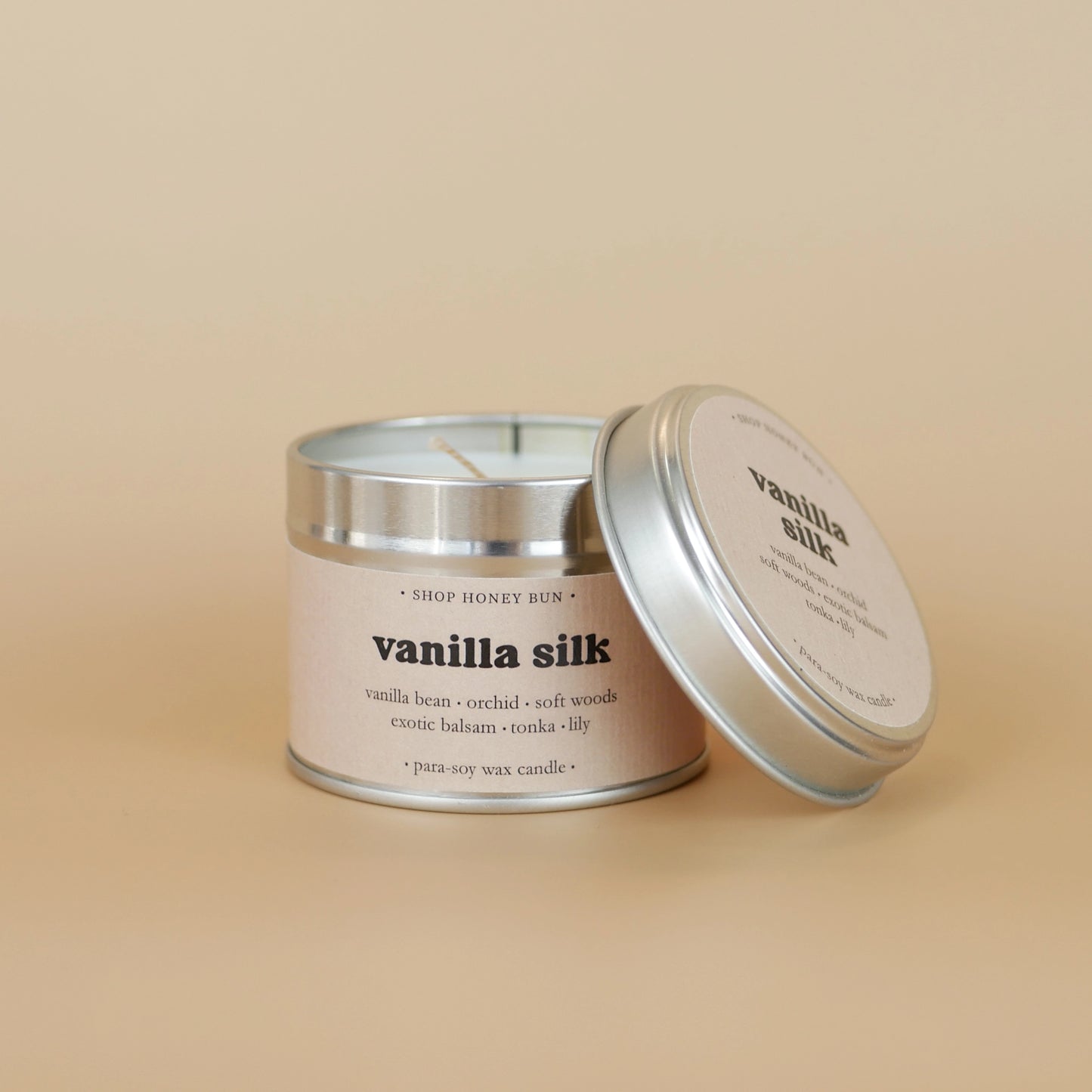 A 20 hour burn time vanilla silk scented tin candle with the lid off, resting on the side of the candle
