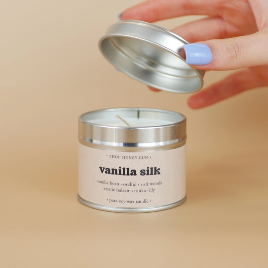 A 20 hour burn time vanilla silk scented in candle with a hand lifting off the lid to show the candle wick