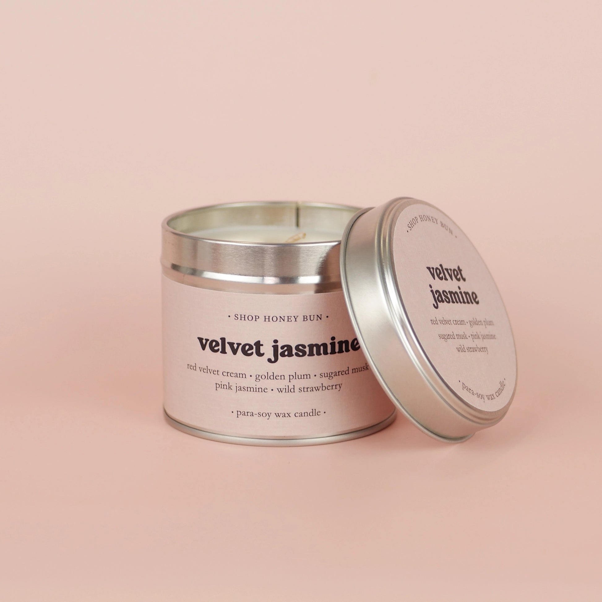A 30 hour burn time velvet jasmine scented tin candle with the lid off, resting on the side of the candle

